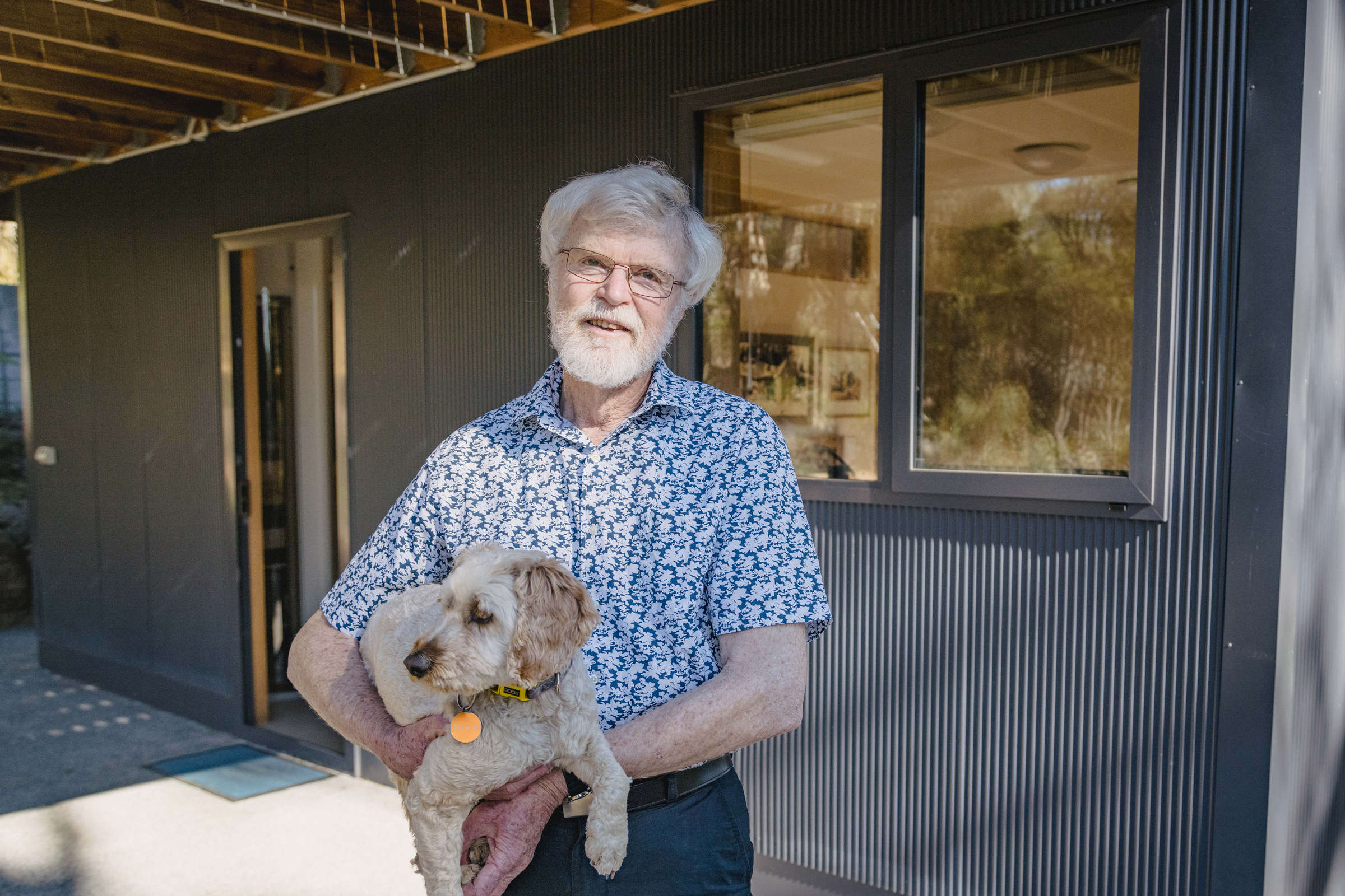 A very happy client holding their cute dog outside the renovated lower level of the house. Externally, the renovation features custom mini orb, double glazed and thermally broken windows and a concrete path exposed aggregate. The renovation was to improve the amenity of the space under the house by building it in, creating two extra bedrooms and a usable under-house storage space. Credit: Jordan Davis.