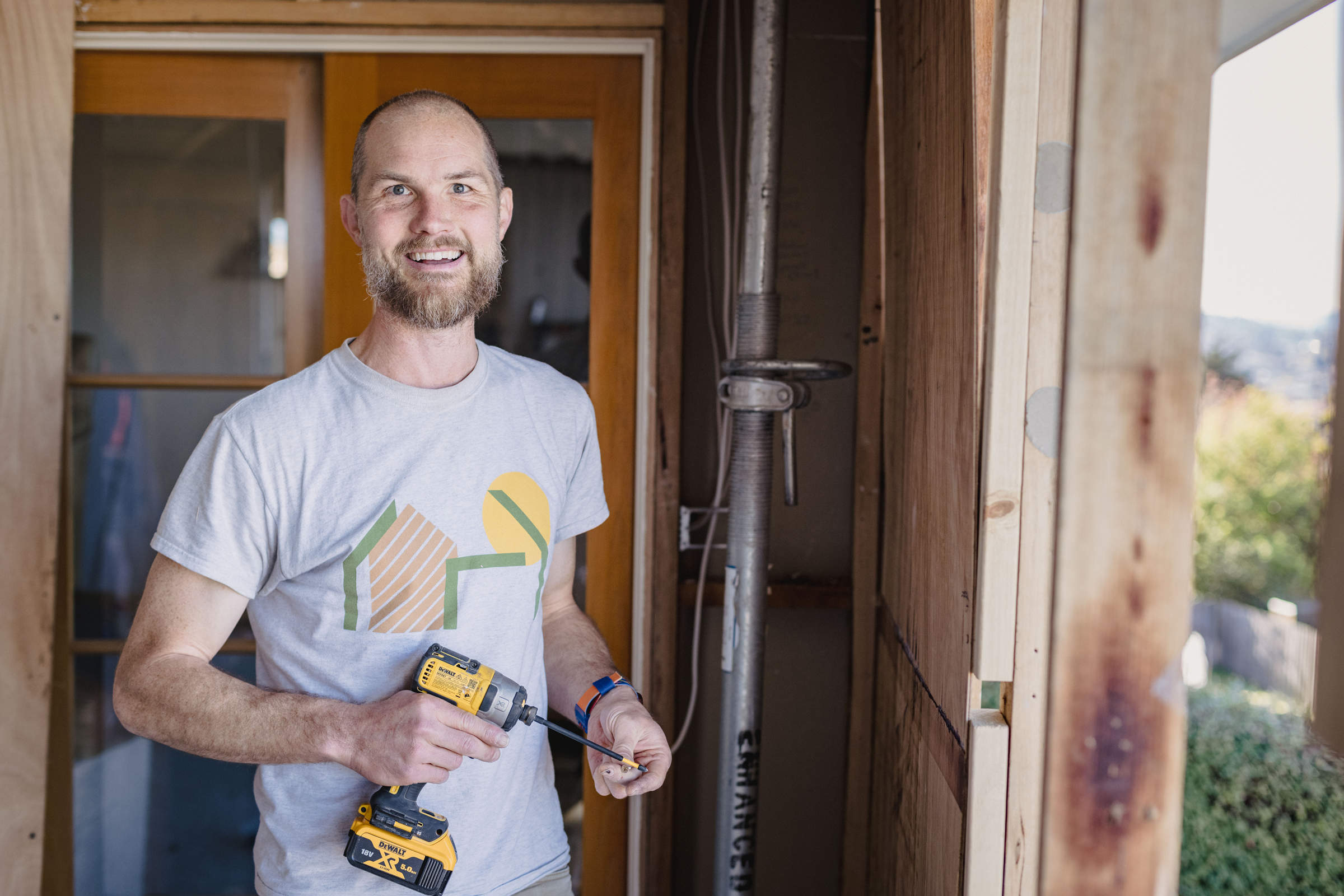 An adult apprentice, holding a drill and working on a home renovation, demonstrating teamwork and a positive team culture. Credit: Jordan Davis.