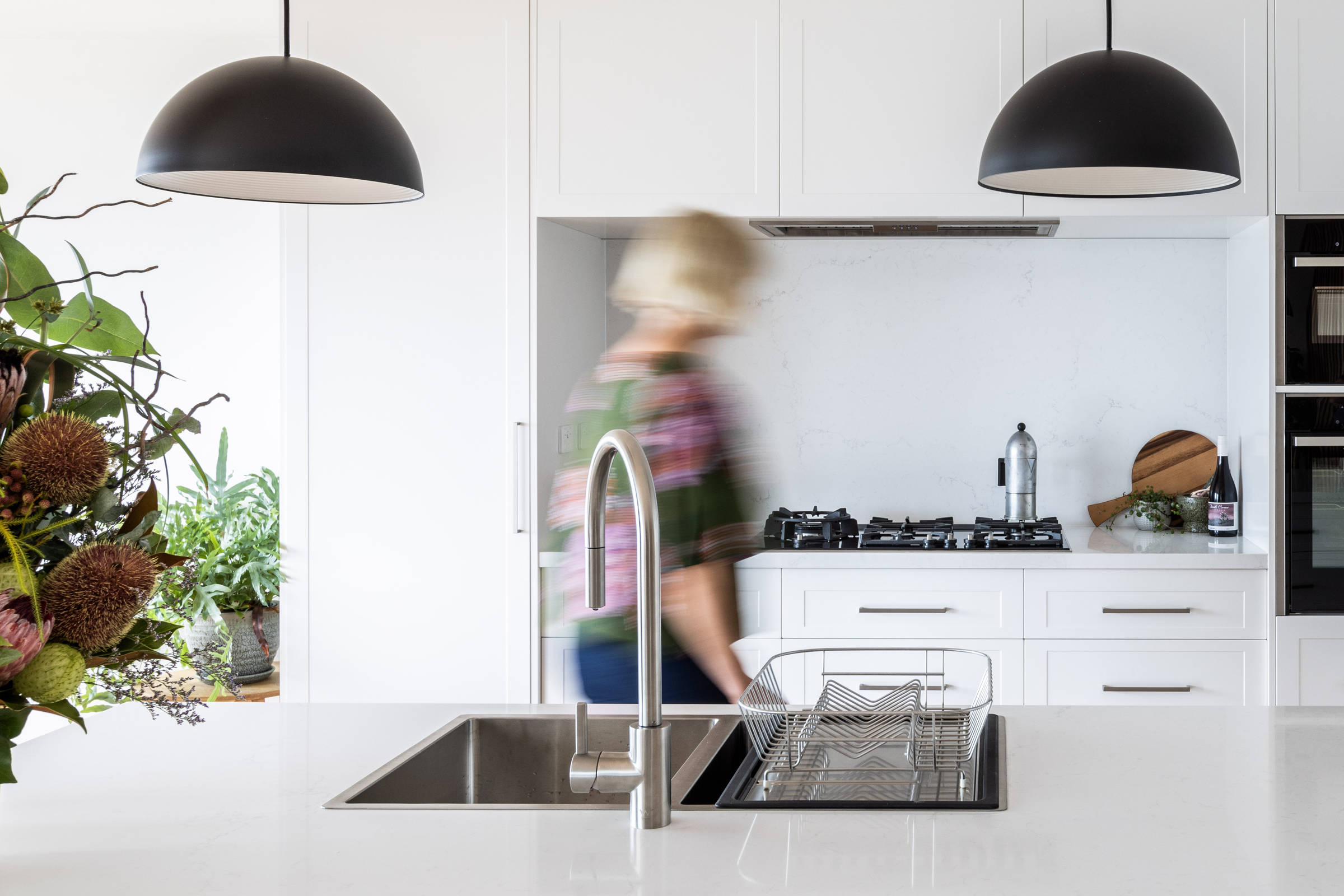 This light and bright, contemporary kitchen renovation has transformed this 1970s house. It features solid stone benchtops, pendant lighting, contemporary lighting, brushed chrome tapware and an in bench sink. Credit: Jordan Davis.