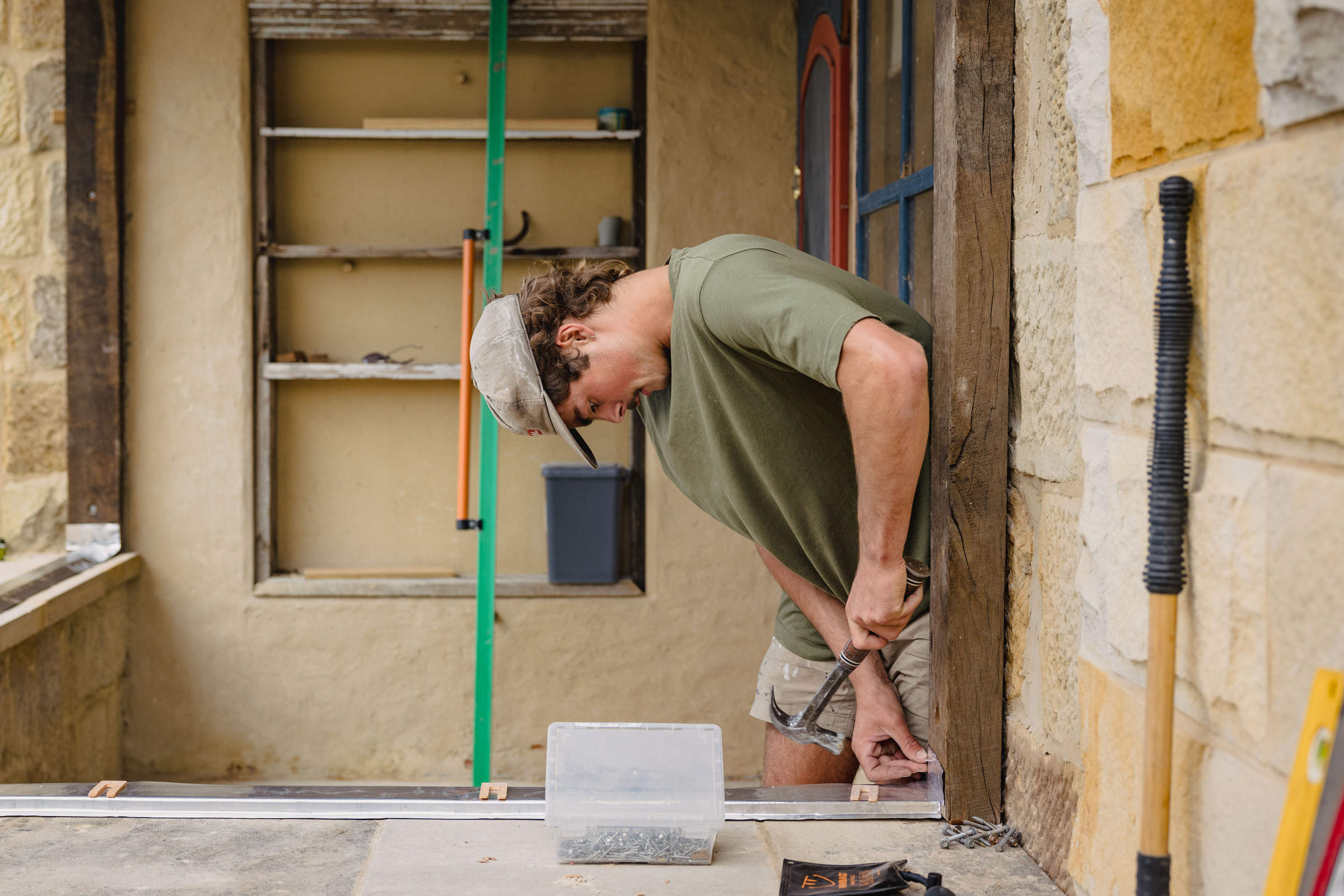 An apprentice working on a home renovation and framing timber studwork against a natural stone wall. Photo: Jordan Davis.