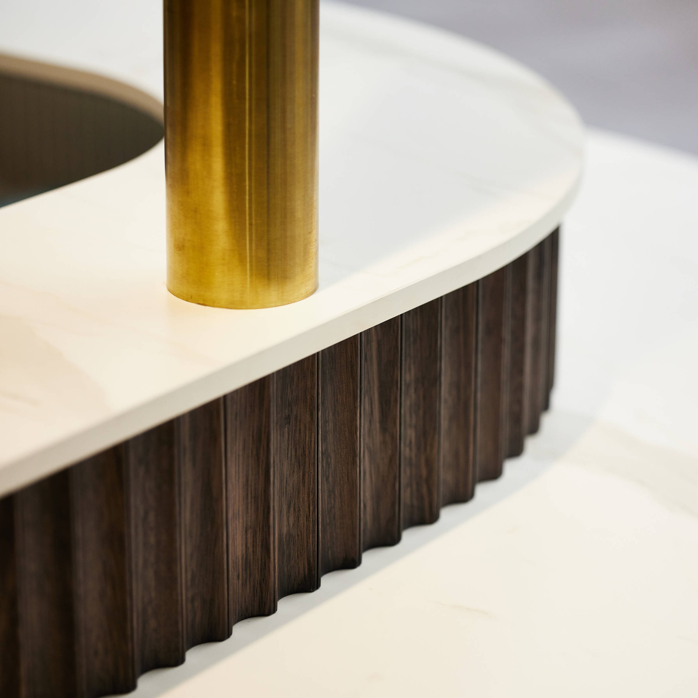 Closeup detail of a brass pole, inset into a white benchtop with dark coloured scalloped feature timber underneath. Credit: Samuel Shelley.