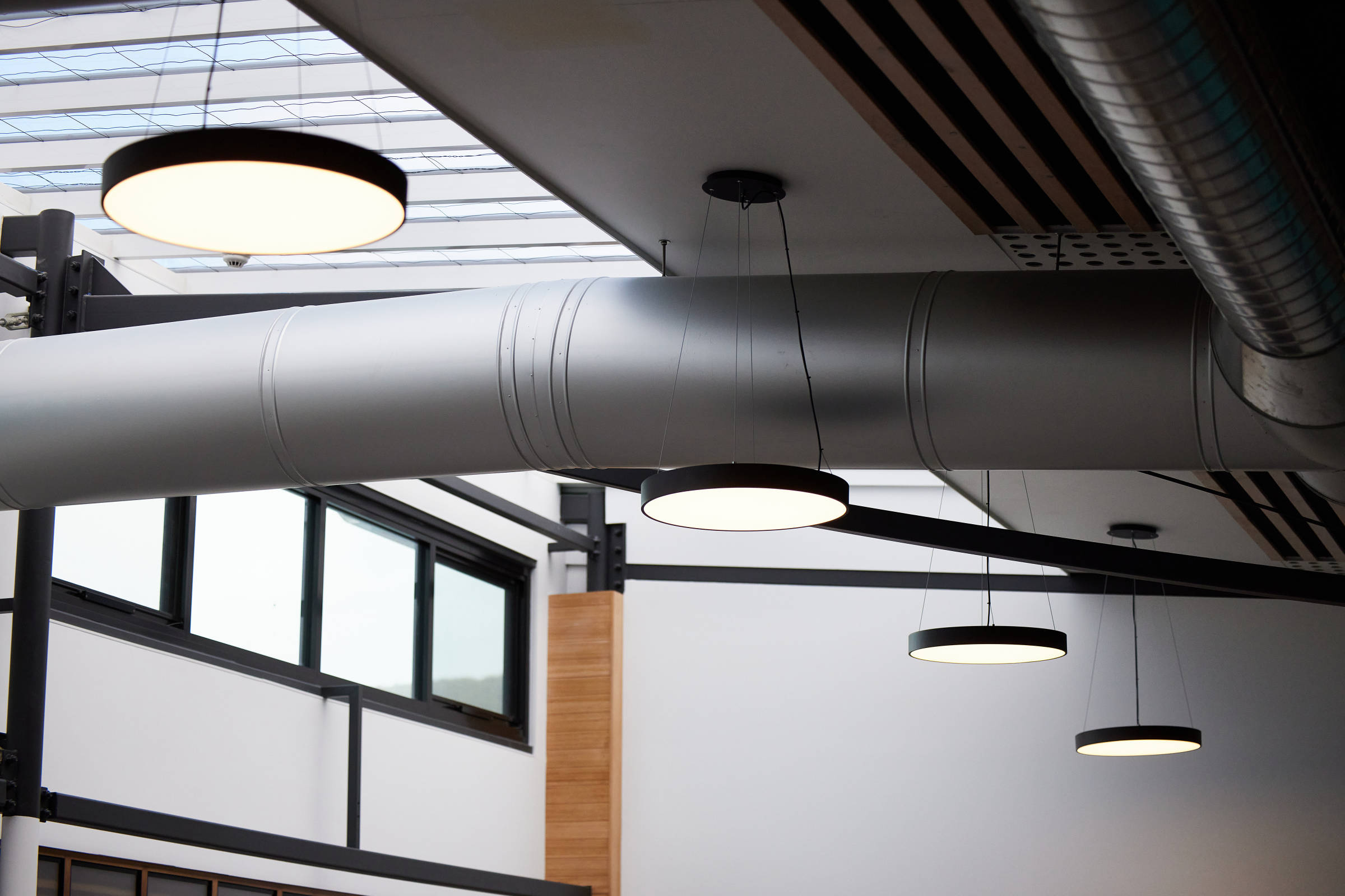 Image of large brushed aluminium matte internal ducting, with two hanging black aluminium circular lights. Credit: Samuel Shelley.