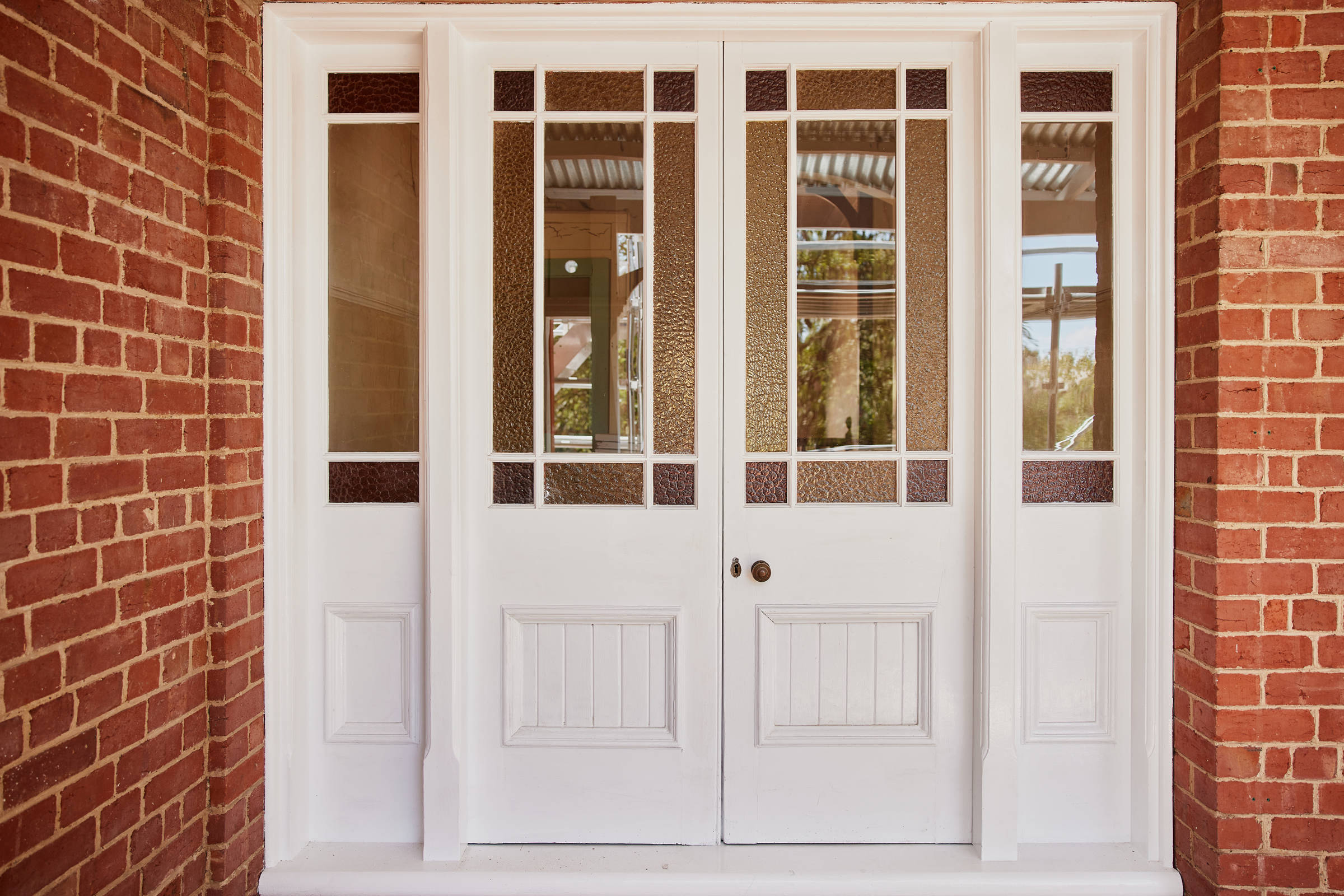 Freshly white painted heritage french doors featuring decorative, rippled glass panels with red brick and white mortar surrounds. Credit: Samuel Shelley.