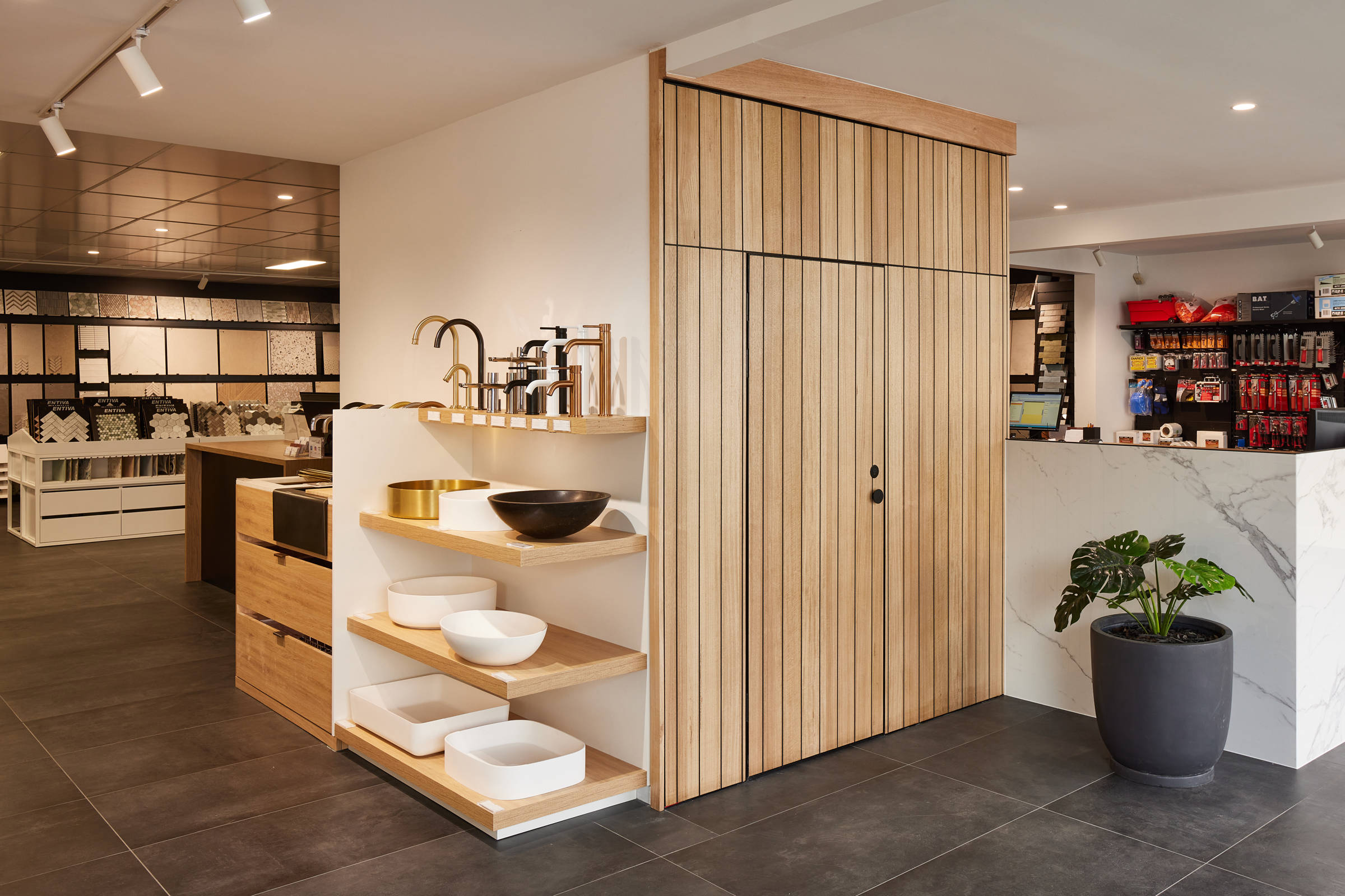 An aspect of the Rossetto Tiles showroom, featuring four timber shelves displaying taps and bathroom basins. The image details neat Tasmanian oak timber panelling for an internal room and the area is bright and well lit. Credit: Samuel Shelley.