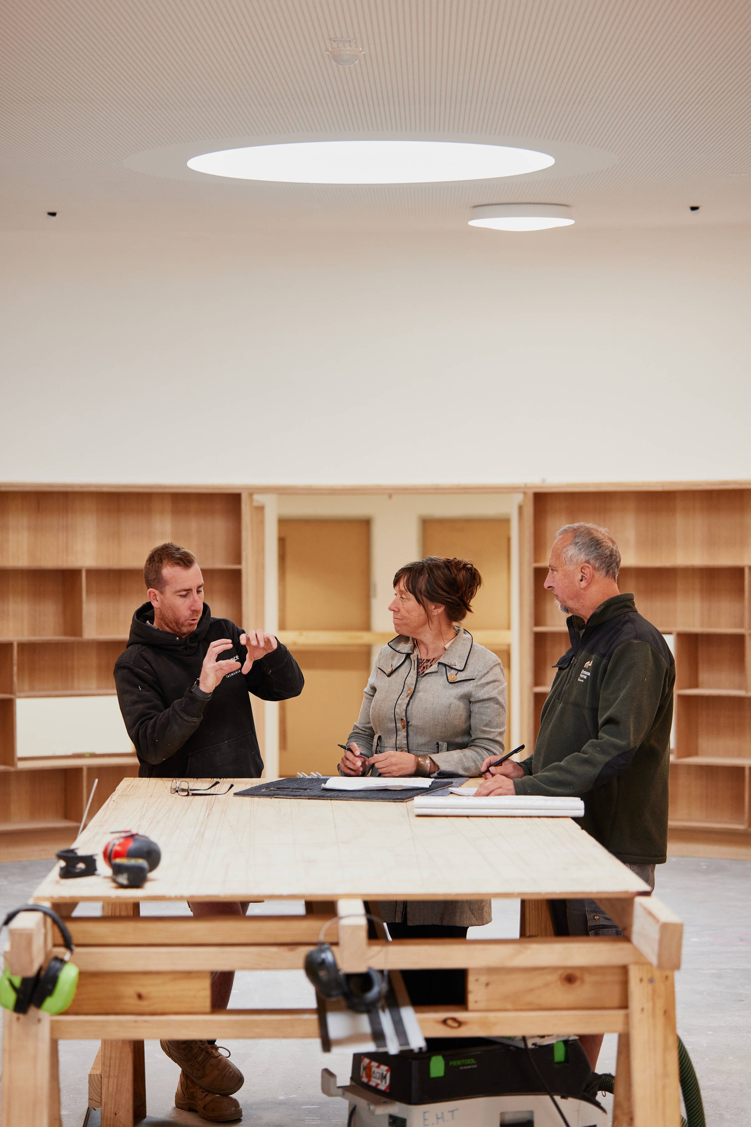 Three people talking about construction detail. The site foreman (a man in his 30s) is gesturing with his hands to demonstrate an idea and he is watched by the architect, a woman in her 50s and the project manager, a man in his 60s. Credit: Samuel Shelley.